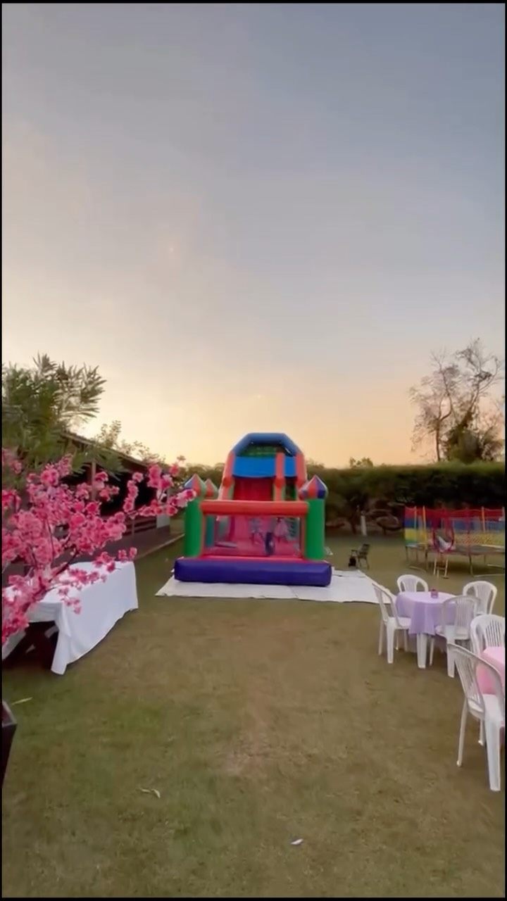 Brinquedo inflável da Tga montado no gramado de uma festa ao entardecer, com mesas e cadeiras ao redor